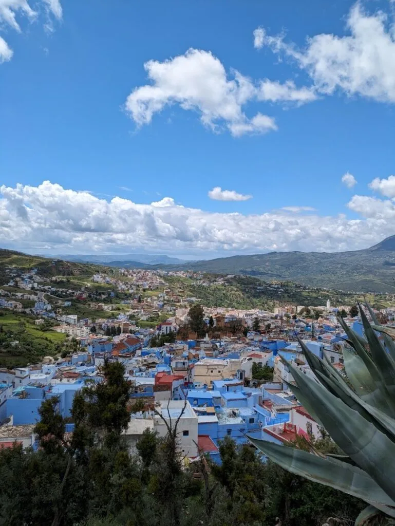 Panoramic view of Chefchaouen's blue-and-white buildings nestled in mountainous landscape with cloudy sky.