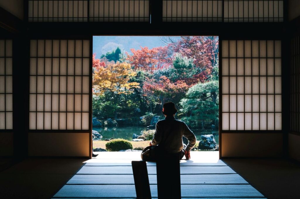 Traditional Japanese ryokan interior with tatami mats and shoji doors framing autumn garden view, perfect for cultural accommodation