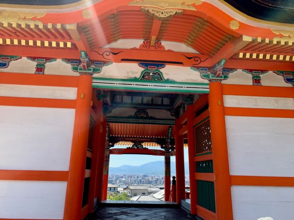 Ornate temple gateway framing Kyoto cityscape view, showcasing traditional vermillion architecture