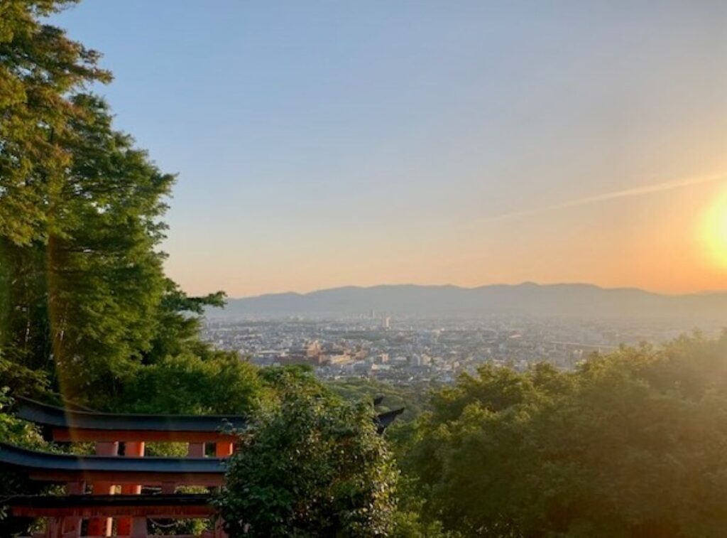 Sunset view over Kyoto city from Fushimi Inari shrine hillside with orange torii gate, magical golden hour stop for your itinerary
