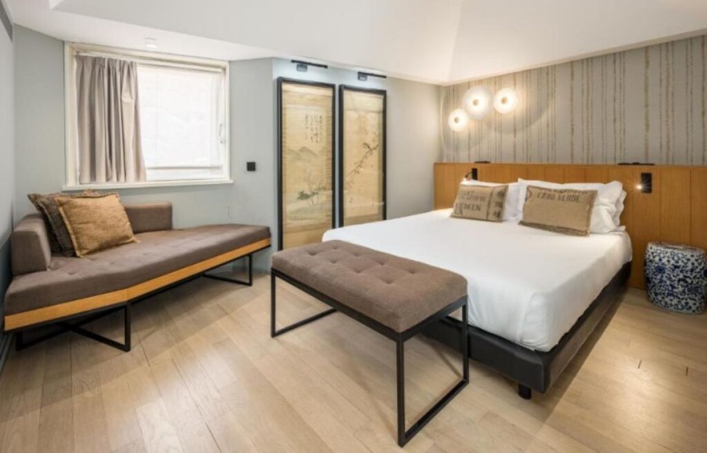 Contemporary hotel suite featuring wooden headboard, separate seating area, and traditional Portuguese artwork on the wall