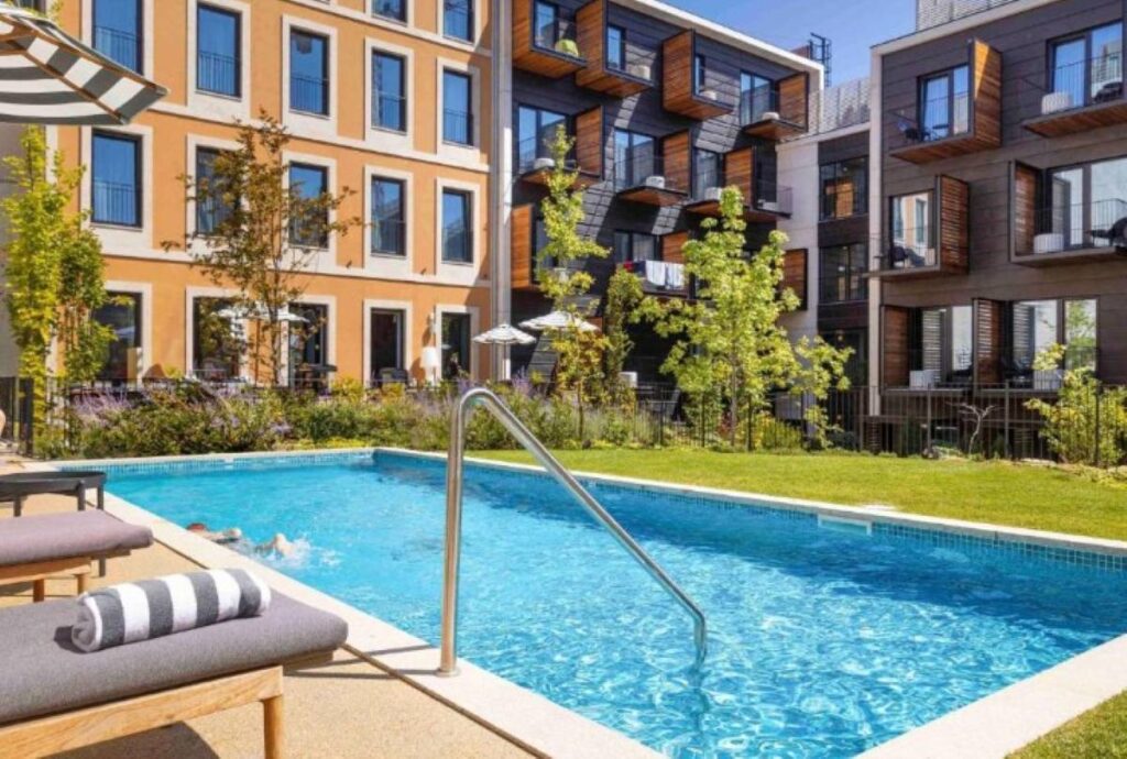 Outdoor swimming pool surrounded by modern apartment-style accommodation with landscaped gardens and wooden balconies