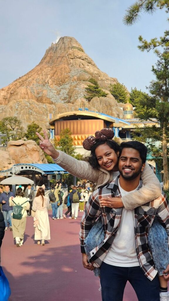 Two visitors posing playfully in front of Mount Prometheus at Tokyo DisneySea.