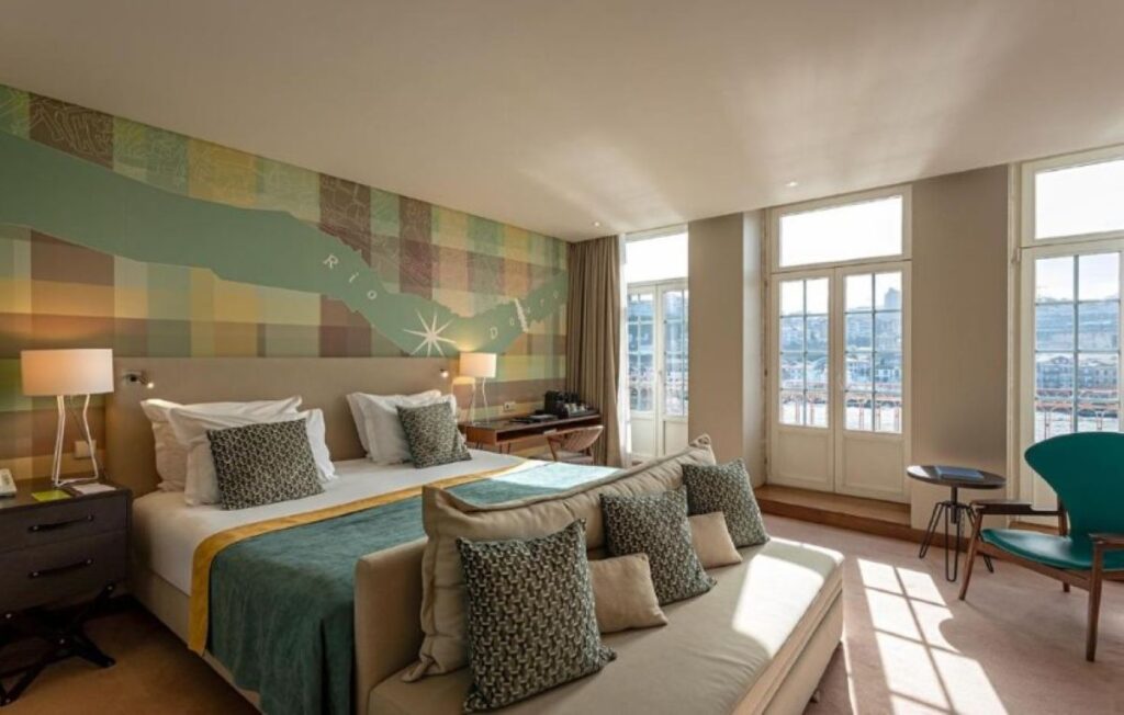 Modern hotel room with colourful mosaic wall art, twin beds, and panoramic city views through floor-to-ceiling windows