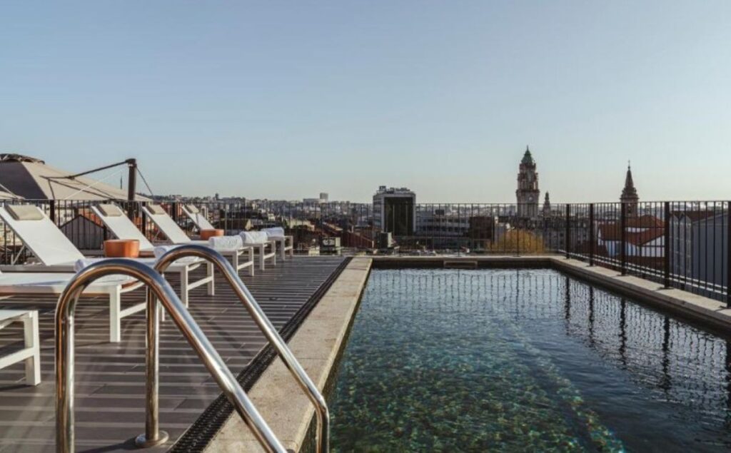 Rooftop swimming pool with wooden decking and sun loungers, offering panoramic views across Porto's historic skyline