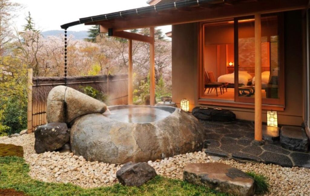 Private open-air rock onsen bath beside ryokan guest room with mountain views