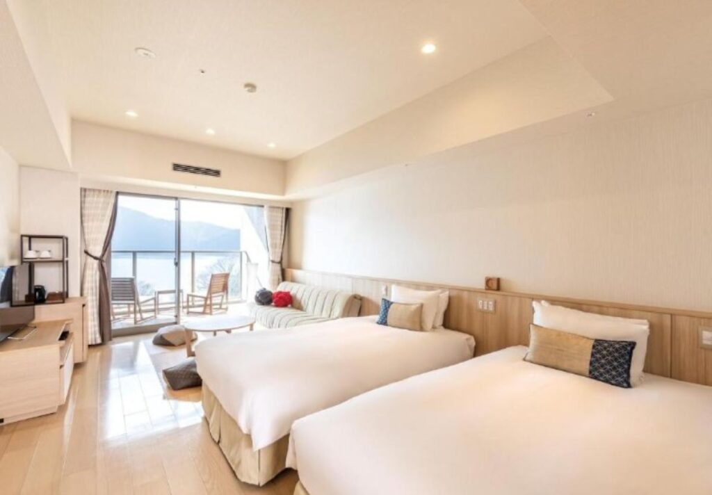 Modern twin-bed ryokan room with mountain views through balcony doors in Hakone