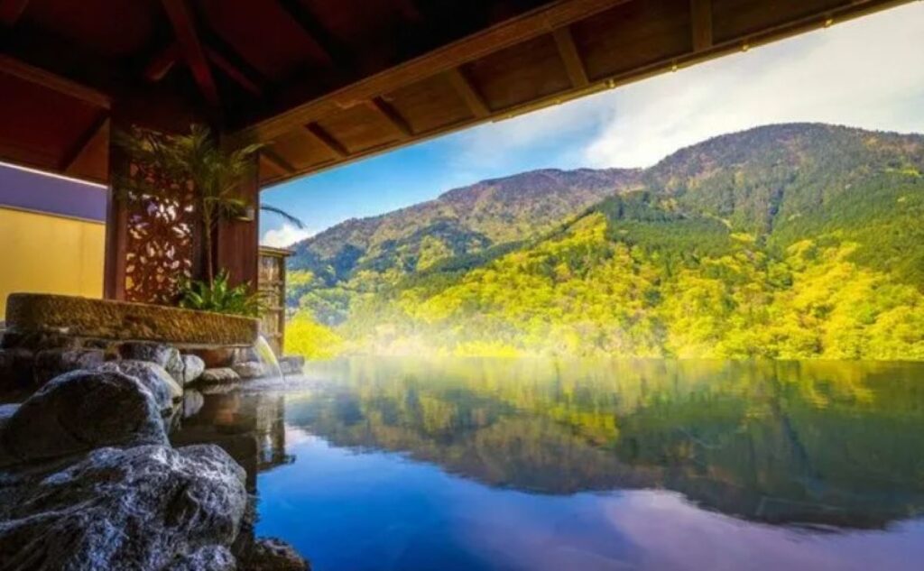 Open-air onsen bath reflecting autumn mountain scenery and vibrant green foliage