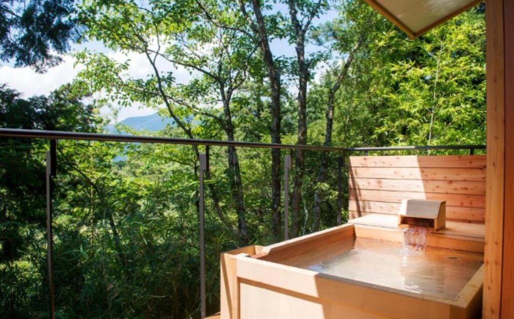 Private hinoki wood onsen bath on balcony overlooking forest canopy at Hakone ryokan