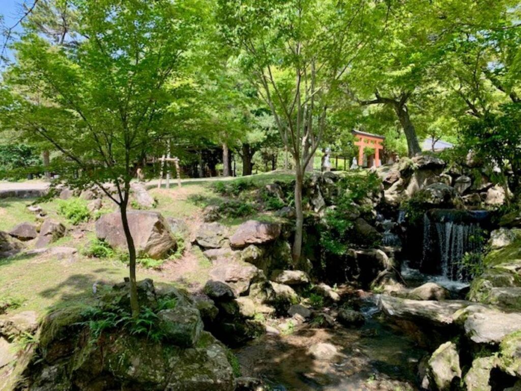 1. Shaded garden in Nara Park, Japan, with a stream and small waterfall beside a red torii gate among maple trees and rocks.