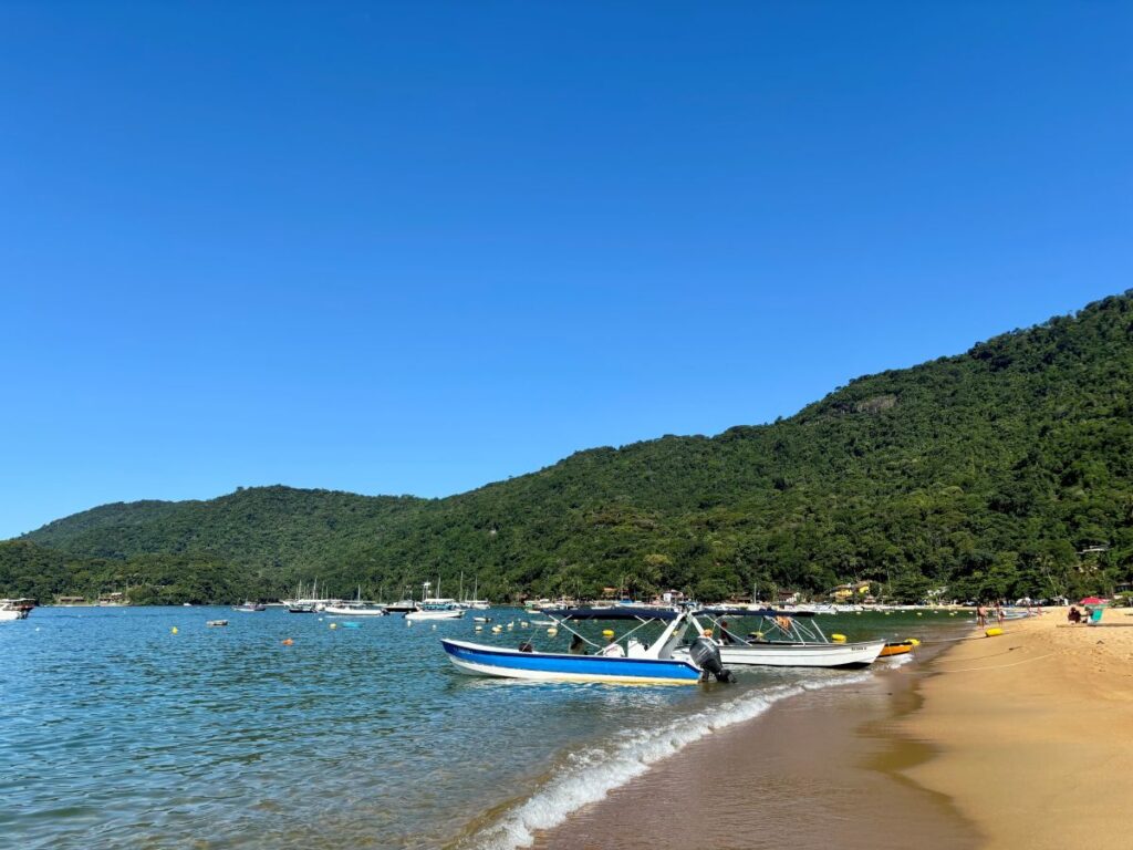 Sandy beach with colourful boats moored in calm bay backed by forested mountains