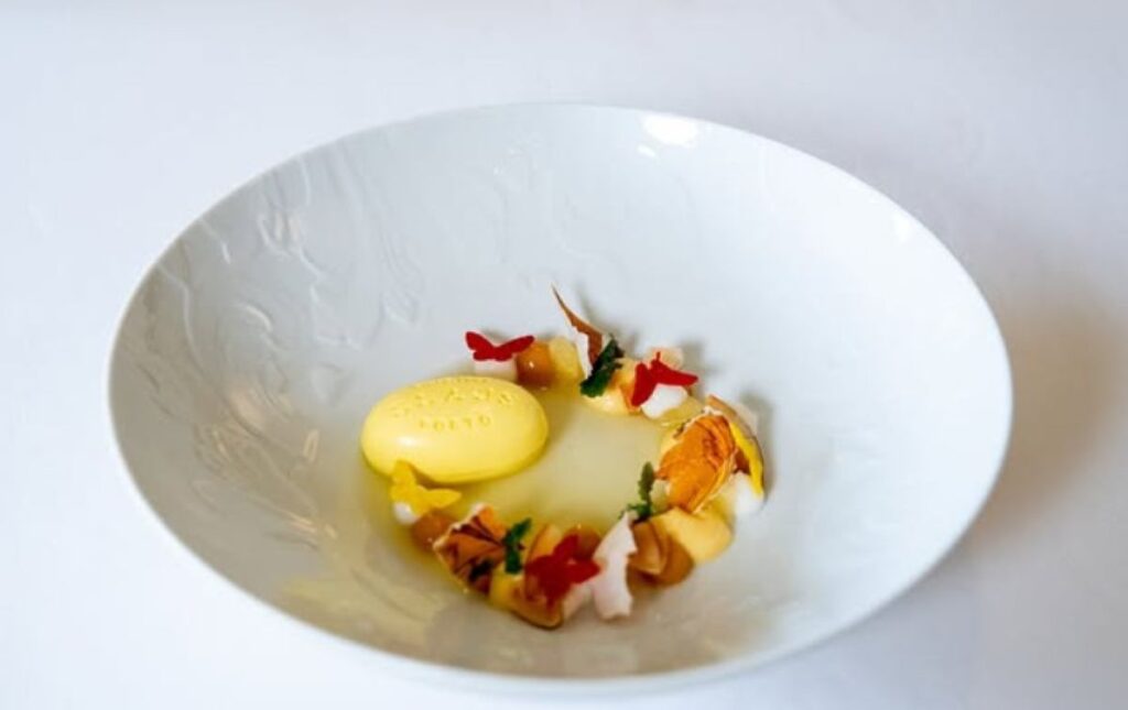 Plated dessert with yellow sorbet, white mousse and delicate garnishes in wide bowl