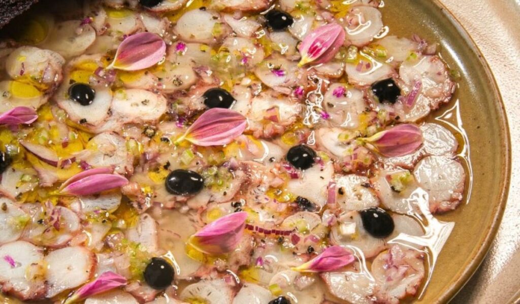 Thinly sliced octopus carpaccio with olive oil, black olives and pink flower petals