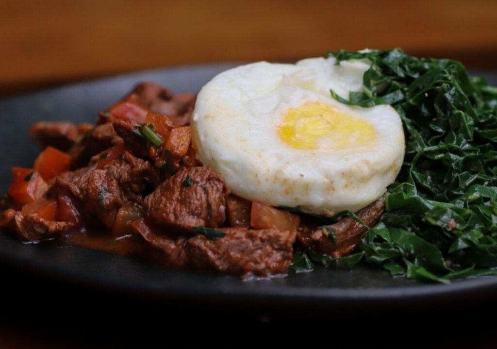 Fried egg served over shredded meat and sautéed kale on dark plate