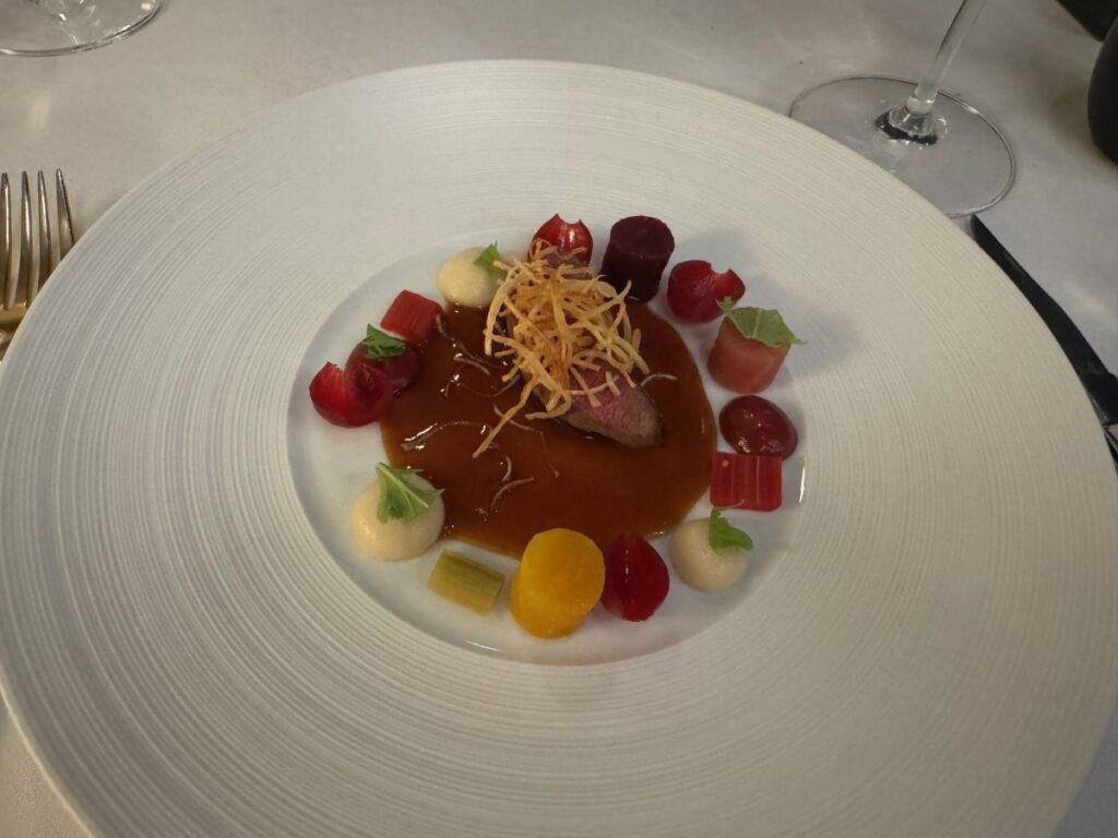 Sliced meat with brown sauce, crispy garnish and colourful vegetable purées on white plate