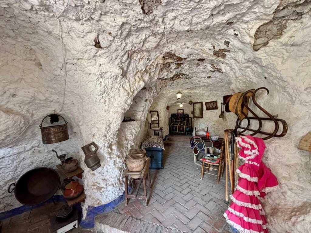 Traditional cave house interior with white rock walls, rustic cookware, framed photos and a pink flamenco dress.
