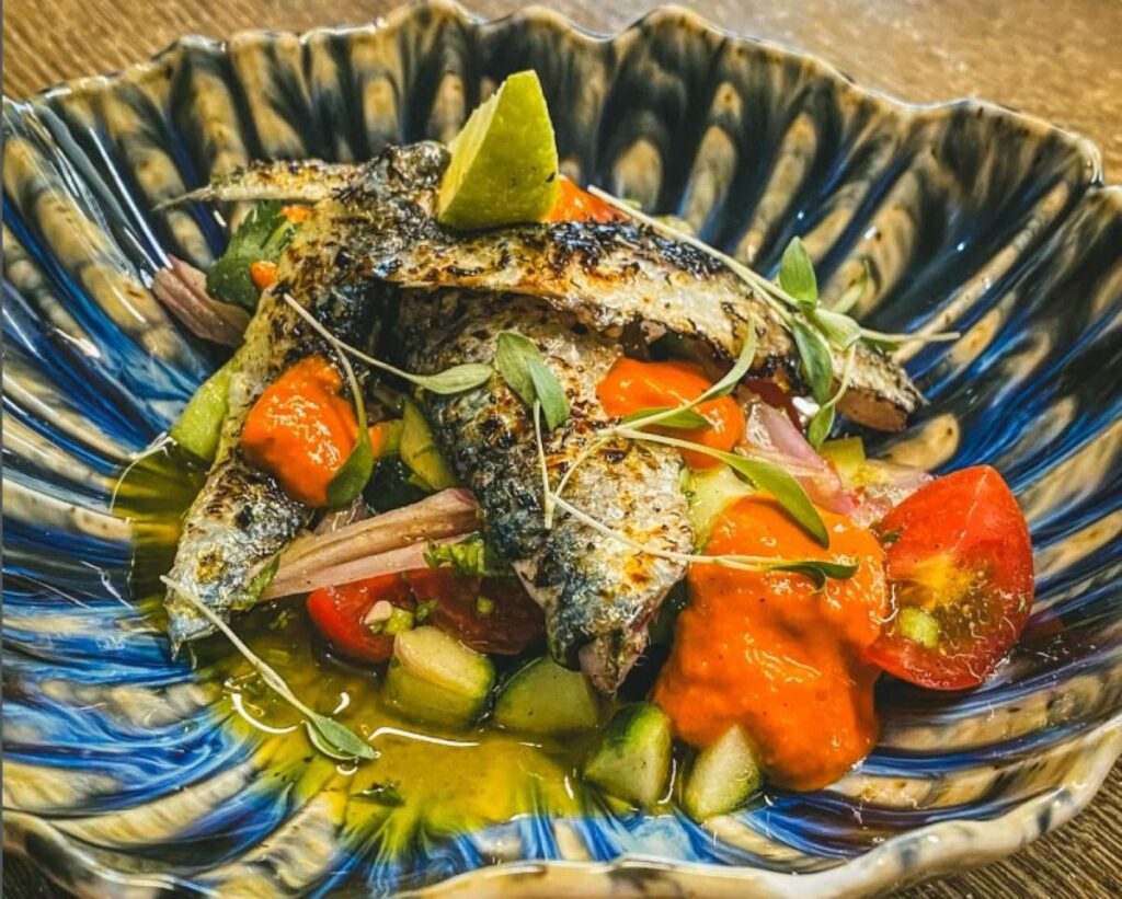 Grilled fish fillet with cherry tomatoes and vegetables in blue patterned ceramic bowl