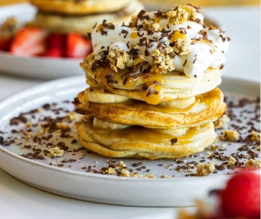 Stack of pancakes topped with whipped cream, banana slices and chocolate shavings