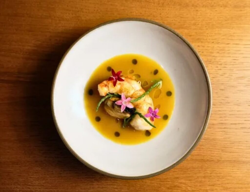 Grilled prawns in golden broth with edible flowers and green beans on white plate