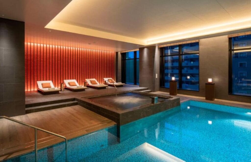 Modern indoor pool with red ambient lighting, loungers and floor-to-ceiling windows at luxury hotel