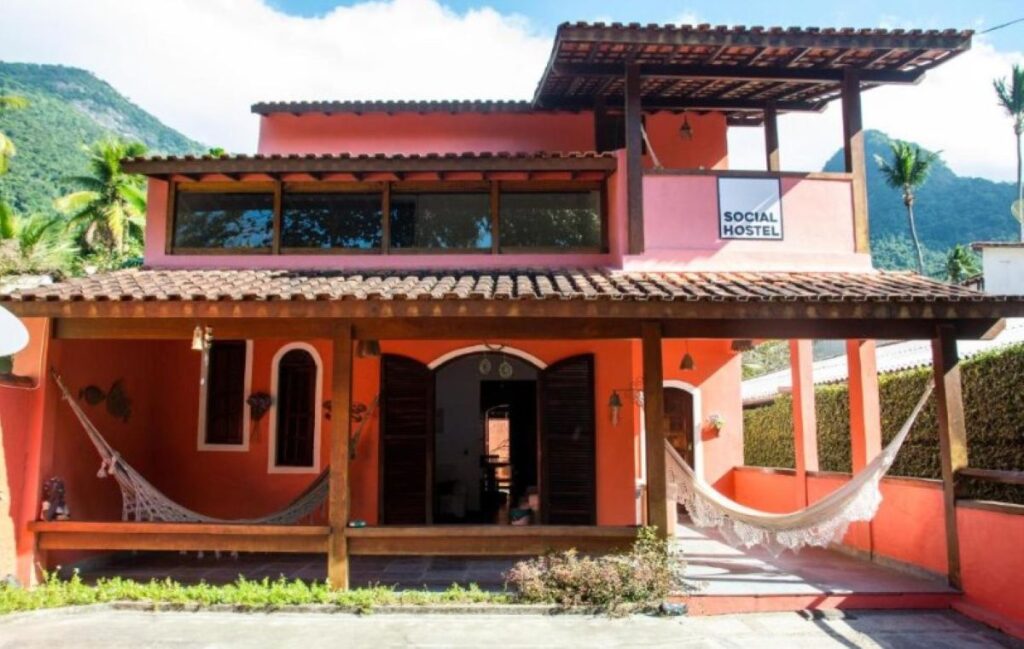 Orange colonial-style pousada exterior with hammocks, terracotta roof and mountain views