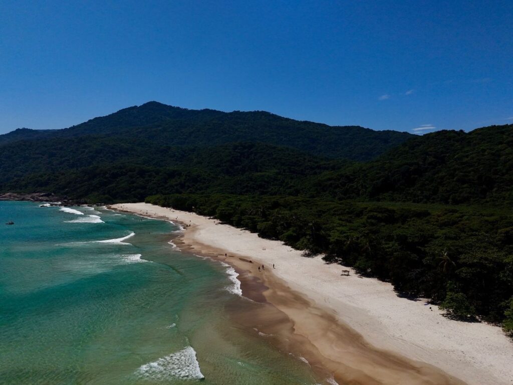 Wide sandy beach on Ilha Grande with turquoise water, gentle waves, and forested hills in the background
