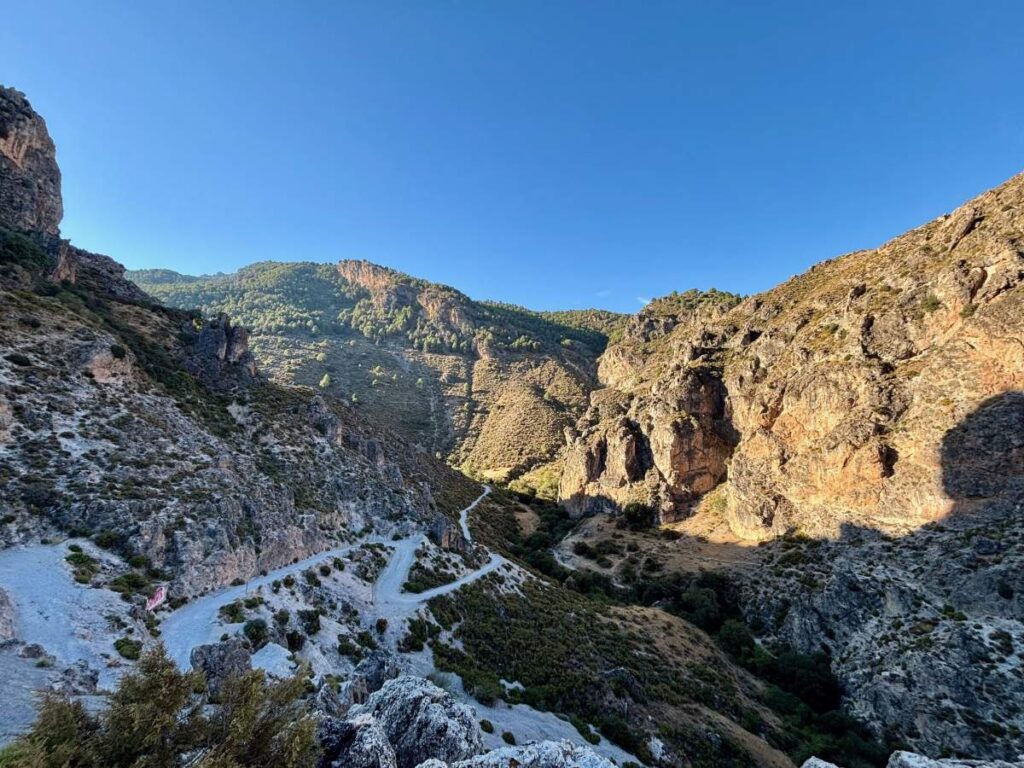 Hiking trail winding through a rugged Sierra Nevada valley with cliffs and forested slopes.