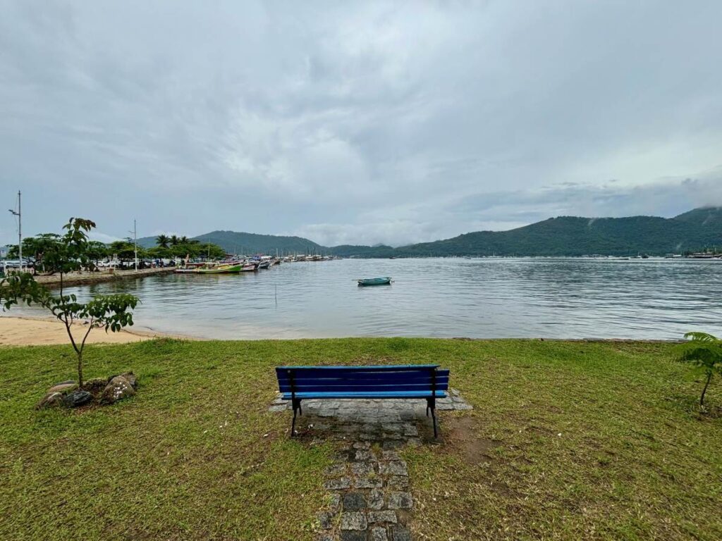 Blue bench overlooking calm bay with mountains and boats in Paraty, Brazil