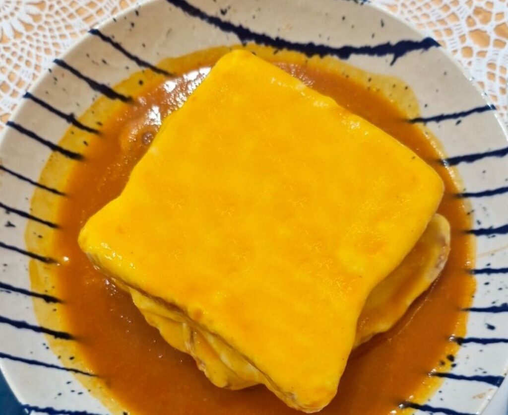 Francesinha on striped ceramic plate with red beer sauce
