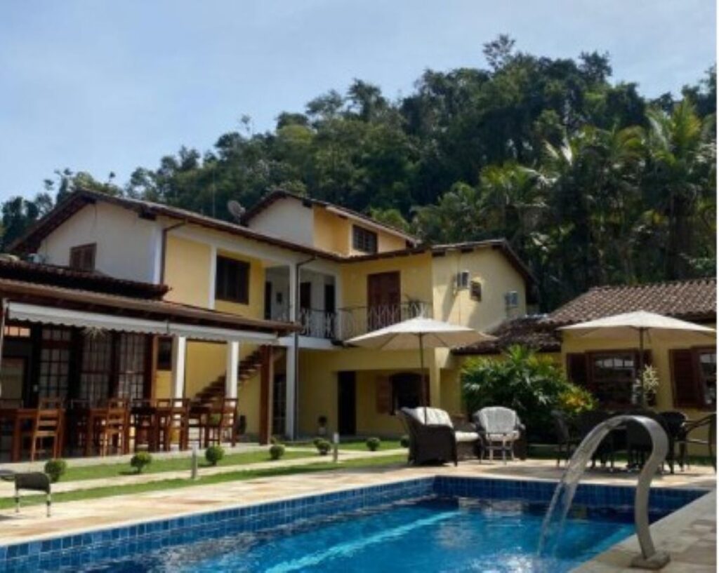 Yellow guesthouse with swimming pool, thatched parasols and rainforest backdrop