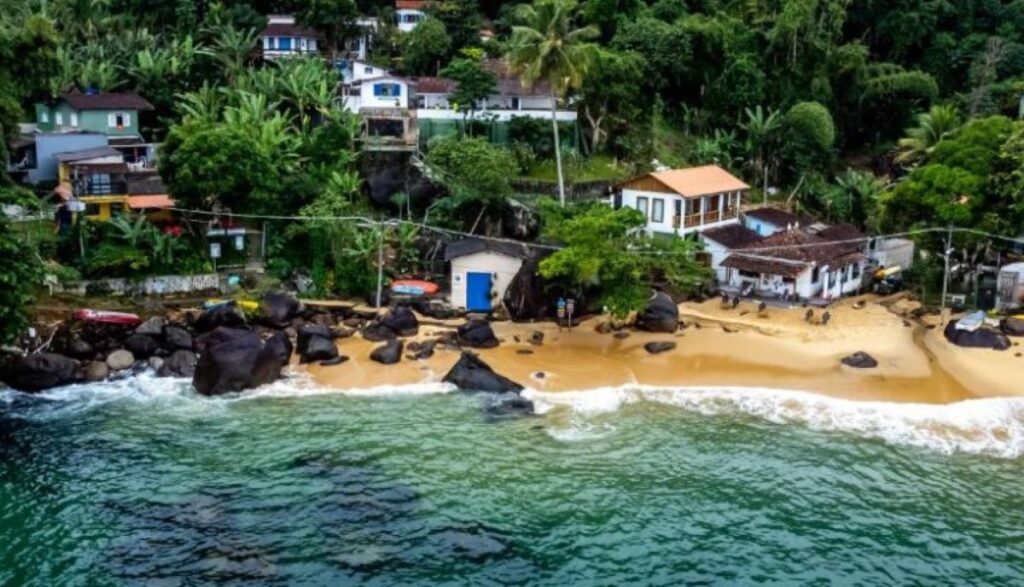Aerial view of small sandy beach with colourful pousadas nestled in tropical hillside