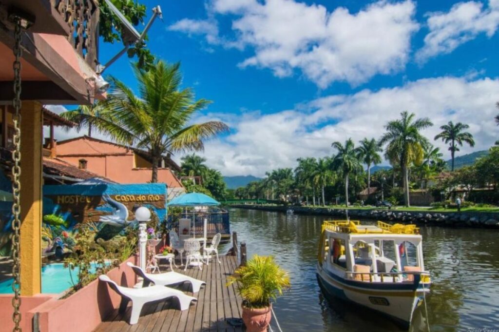 Waterfront hostel with wooden deck, palm trees and tour boat on sunny canal