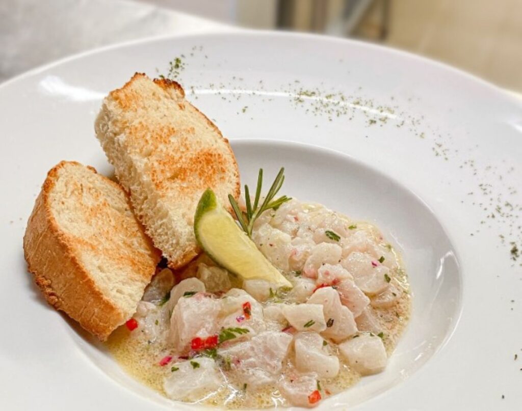 White fish ceviche with toasted bread slices, lime wedge and chilli flakes