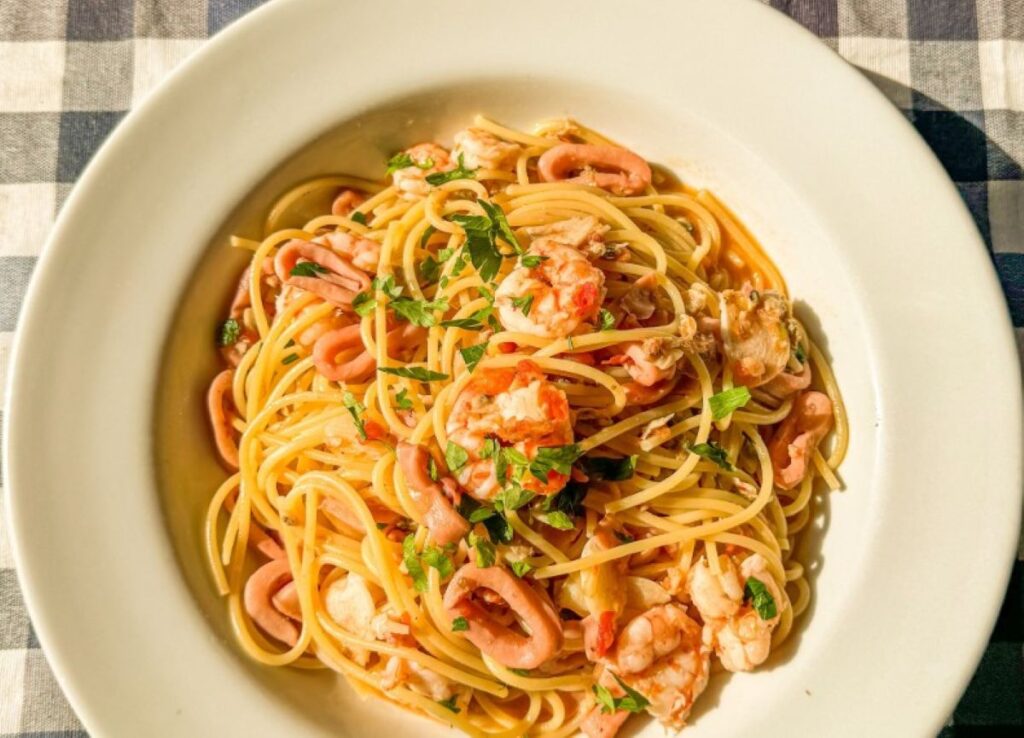 Spaghetti tossed with prawns, squid and fresh parsley in white bowl