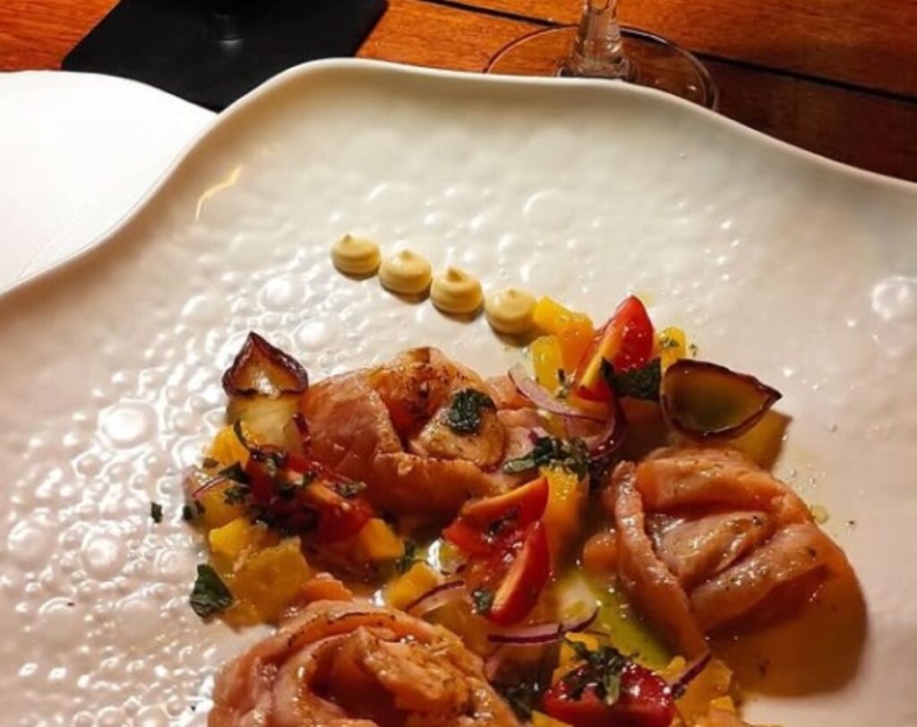 Seared seafood with colourful peppers, tomatoes and dots of aioli on decorative plate