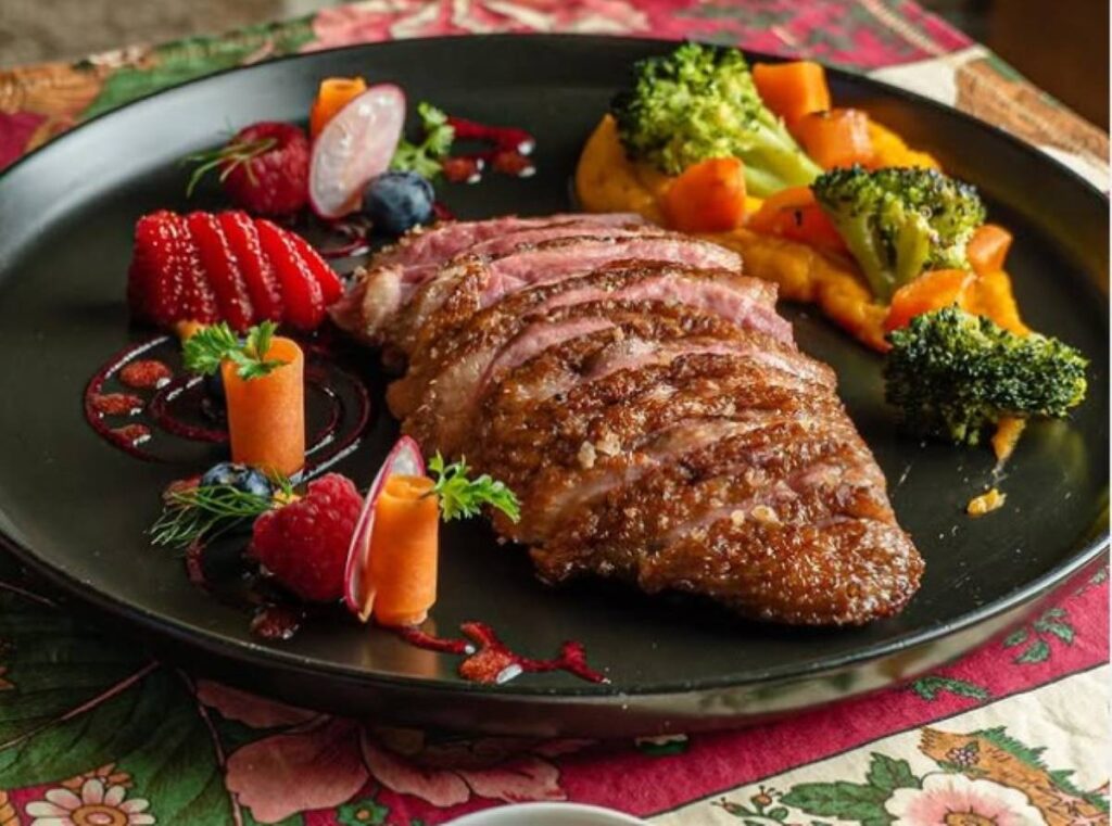 Sliced roasted meat with broccoli, peppers and berry garnish on black plate