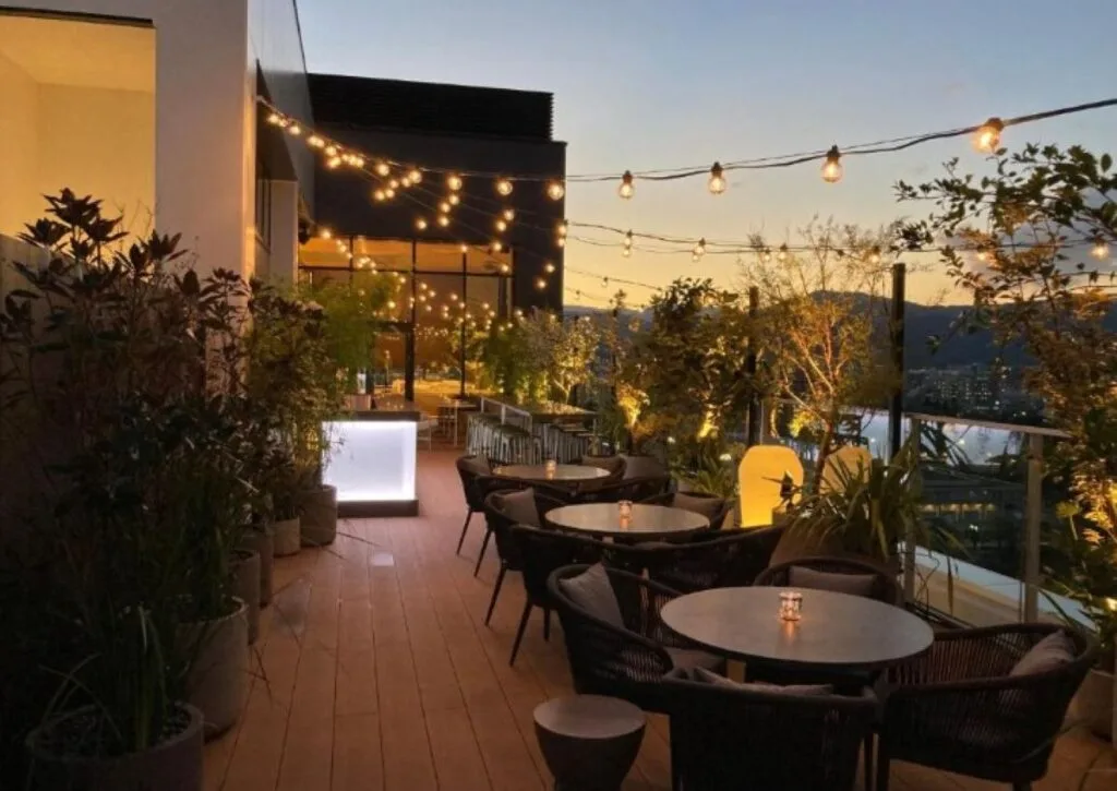 Rooftop terrace bar at sunset with string lights, seating areas and city views