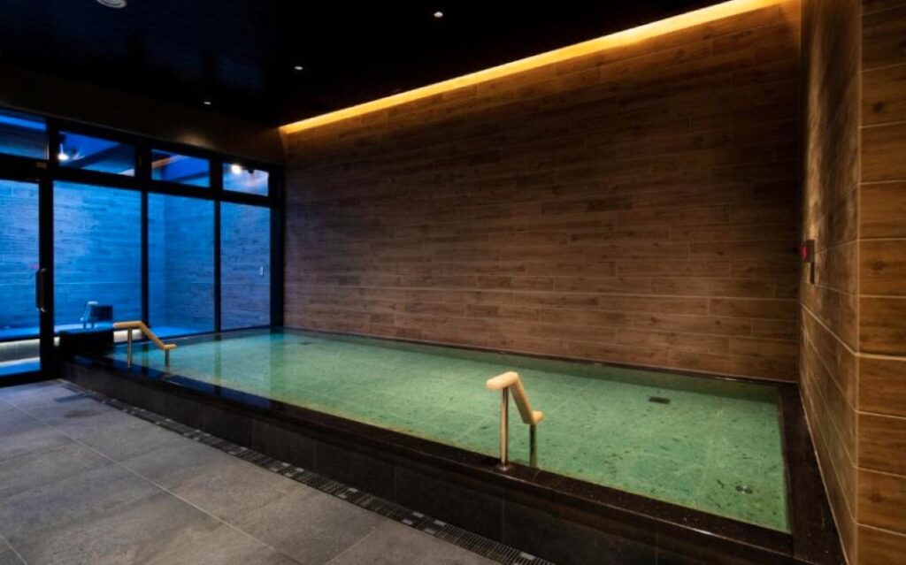 Indoor onsen bath with wooden walls and floor-to-ceiling windows at Japanese hotel
