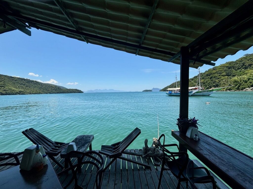 View from a waterfront deck with wooden chairs overlooking calm turquoise water and anchored boats