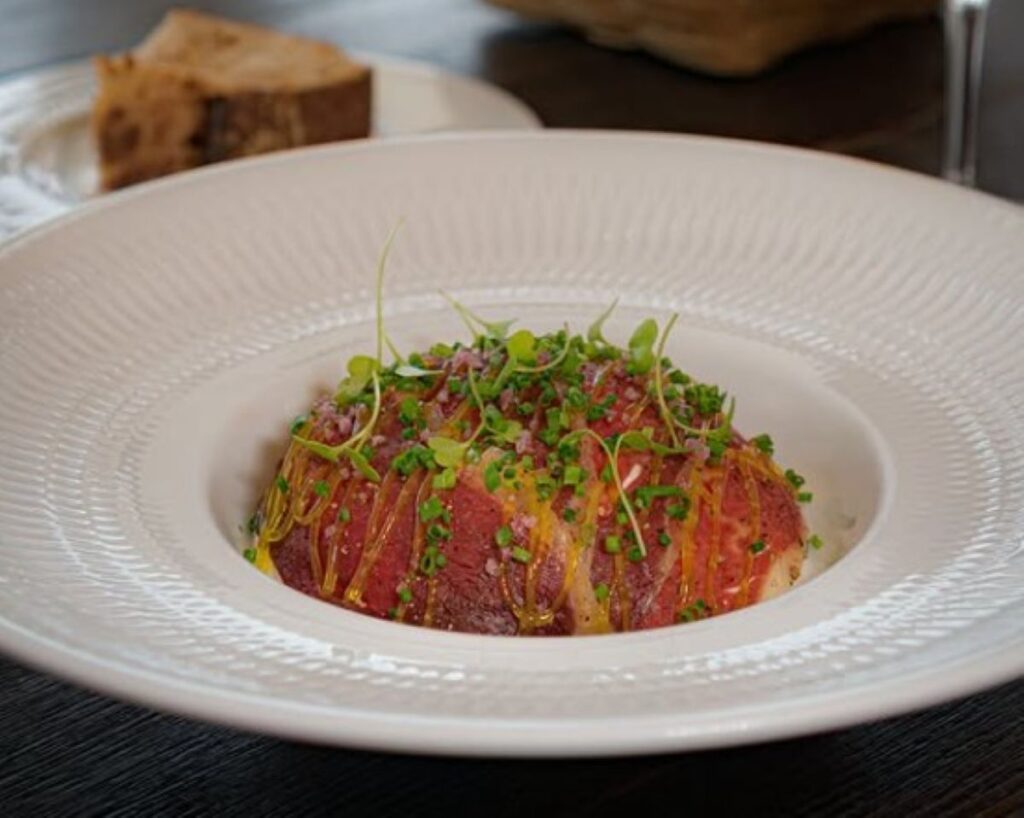 Thinly sliced raw beef topped with fresh herbs, microgreens and olive oil drizzle