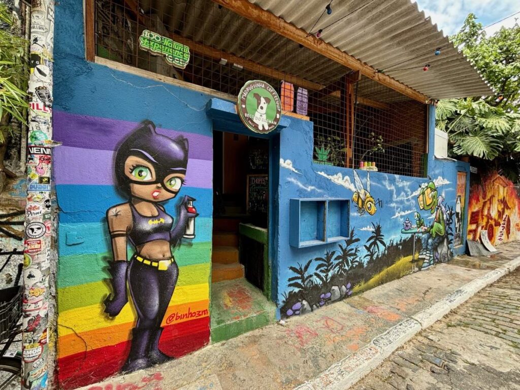 Colourful street art mural on a blue wall, painted characters and scenes along a cobbled lane