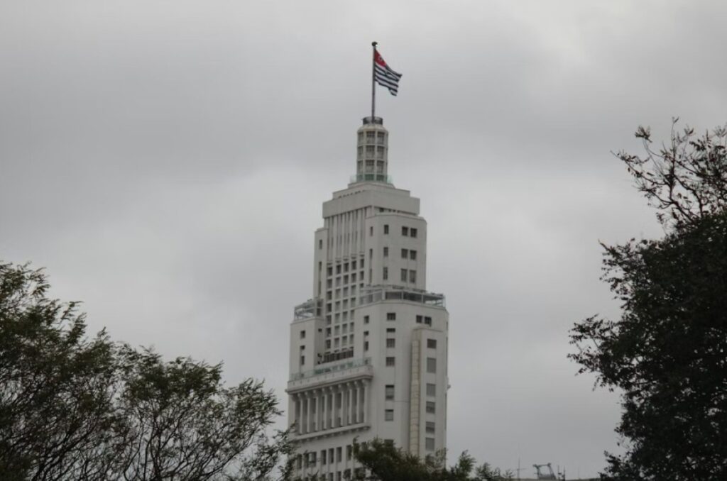 Farol Santander (Altino Arantes Building) rising above trees, topped with the São Paulo state flag