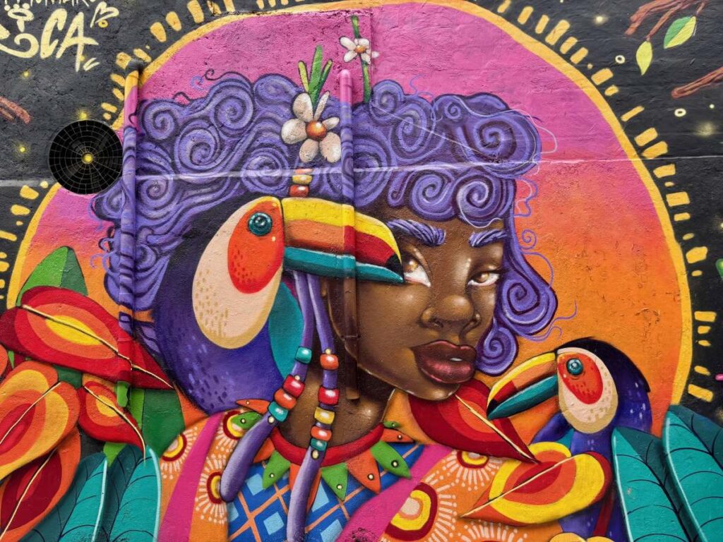Bright mural of a woman with purple hair and toucans, painted in vivid colours on a street art wall