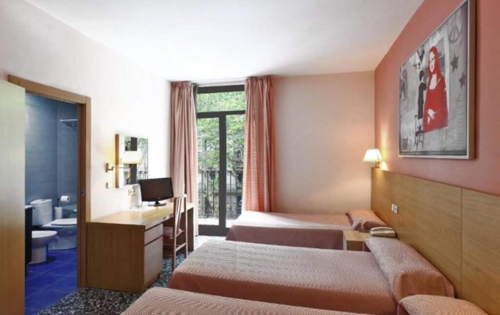 Budget twin room with coral pink walls, bold pop art print, balcony with tree views and en-suite bathroom