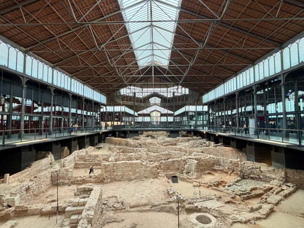El Born Cultural Centre interior, showing the iron-and-glass hall above excavated stone ruins and walkways.