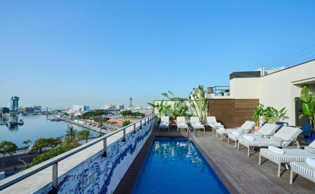 Rooftop lap pool with striped sun loungers, tropical plants and sweeping views over the harbour and marina