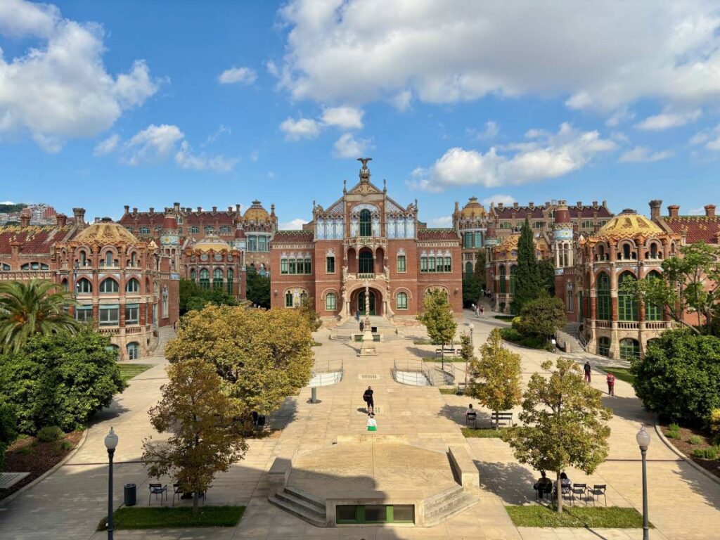 View across the central courtyard of Hospital de Sant Pau, with tiled domes, red brick wings and landscaped paths.