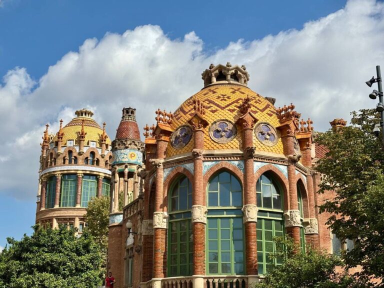 Art Nouveau domes and brickwork at Hospital de Sant Pau, with tiled roofs, arched windows and trees in front.