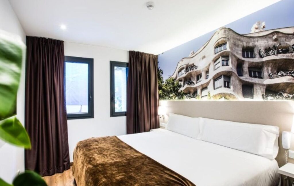 Compact double room with oversized Casa Milà photographic mural headboard, dark curtains and wooden floors