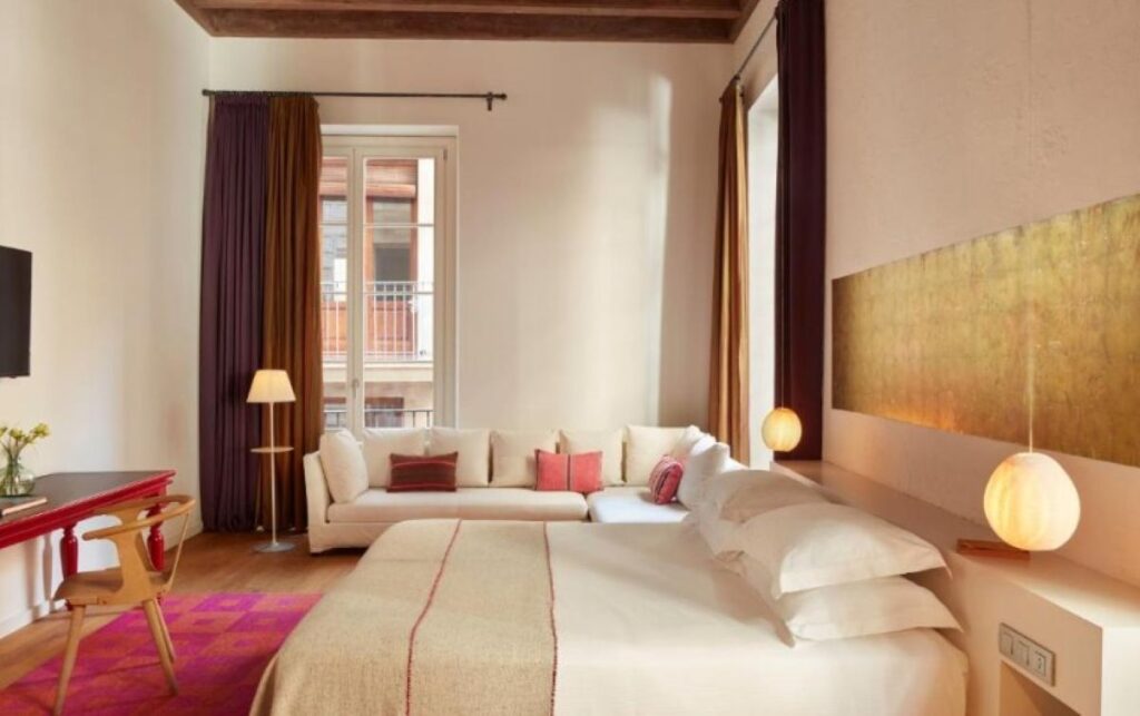 Spacious suite with exposed timber beam ceiling, large gold wall artwork, vibrant pink rug and tall French windows